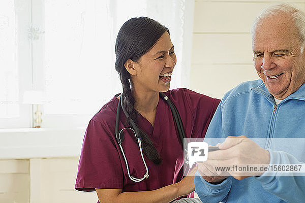 Ein älterer Mann benutzt ein Mobiltelefon  während eine lächelnde junge Krankenschwester zuschaut