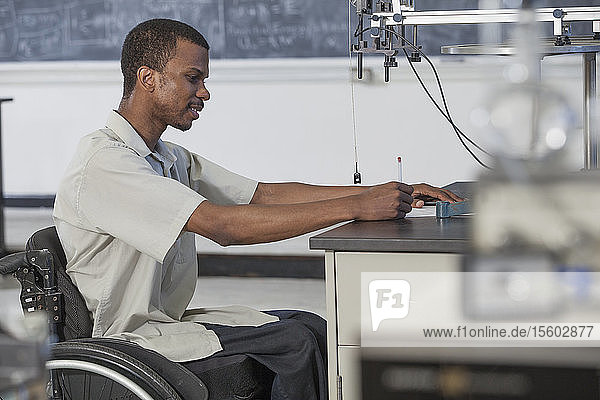 Student with Spinal Meningitis in wheelchair studying acceleration on a frictionless table in laboratory