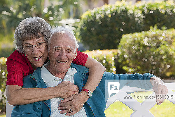 Porträt einer älteren Frau  die ihren Mann in einem Park von hinten umarmt