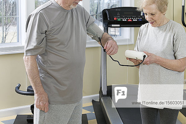 Die Ehefrau prüft den Blutdruck ihres Mannes im Fitnessstudio.