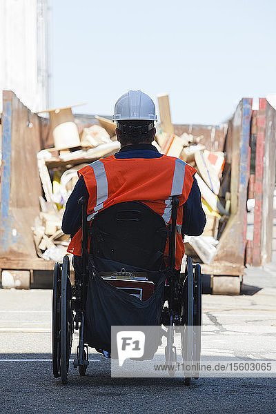 Gebäudetechniker im Rollstuhl mit Rückenmarksverletzung nähert sich einem Müllcontainer