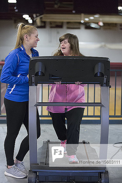 Young woman with Down Syndrome working out with her trainer on an exercise machine in gym