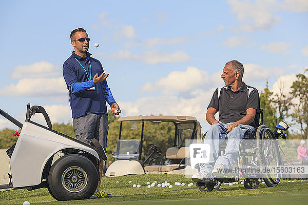 Mann mit Rückenmarksverletzung in einem adaptiven Wagen  der zusammen mit seinem Assistenten Golf spielen soll
