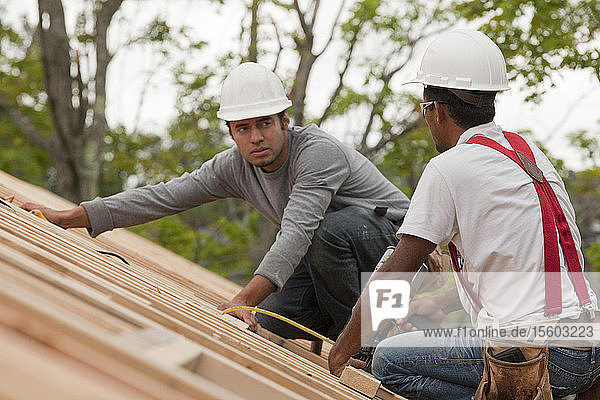 Hispanische Zimmerleute arbeiten mit einer Nagelpistole auf dem Dach eines im Bau befindlichen Hauses