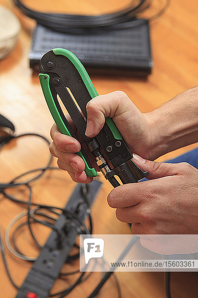 Kabelinstallateur  der mit einer Crimpzange einen neuen Kabelstecker an ein Kabel anbringt