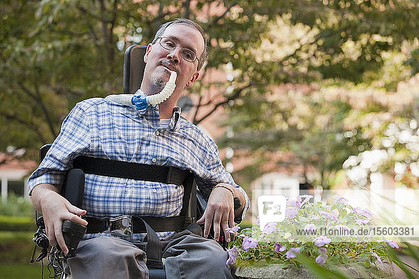 Mann mit Duchenne-Muskeldystrophie im Rollstuhl sitzend mit einem Beatmungsgerät