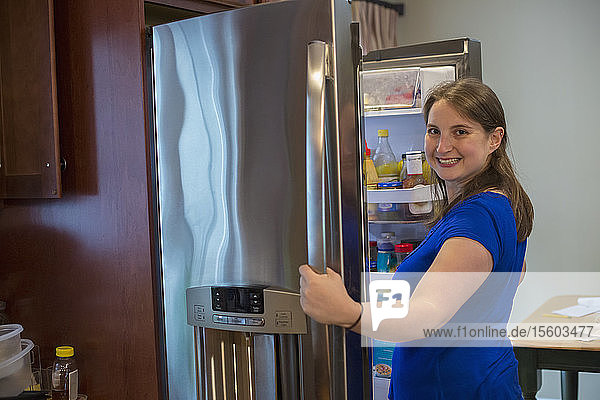 Junge Frau mit zerebraler Lähmung öffnet Kühlschrank zu Hause