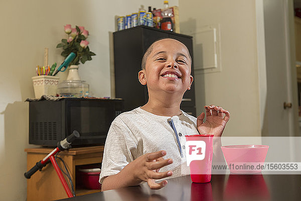 Glücklicher hispanischer Junge mit Autismus beim Essen in seiner Küche