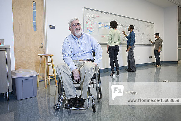 University professor with Muscular Dystrophy in a wheelchair with his students in the background