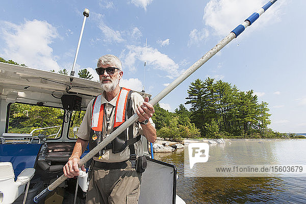 Public works engineer on service boat holding a boathook to grab mooring