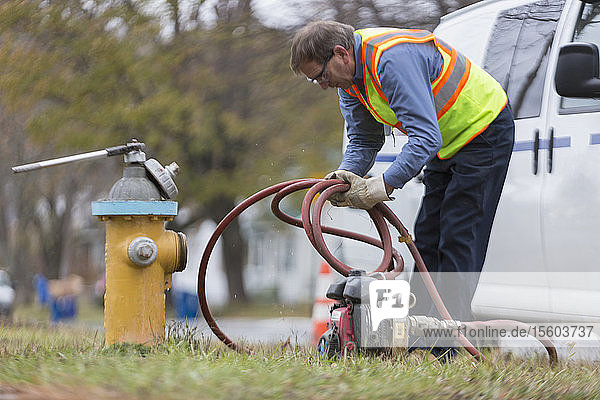 Ein Techniker der Wasserbehörde rollt einen Schlauch auf  um einen Hydranten zu spülen.