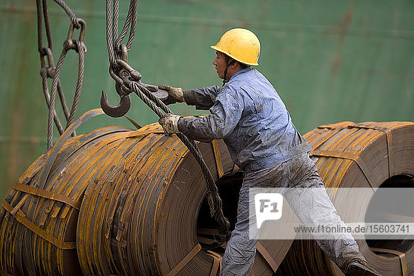 Männlicher Bauarbeiter  der in einer Werft Kabel an Metallspulen befestigt