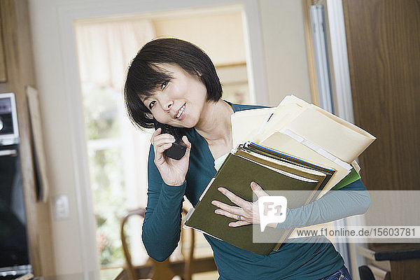 Porträt einer erwachsenen Frau  die einen Stapel Akten hält und mit einem Mobiltelefon spricht