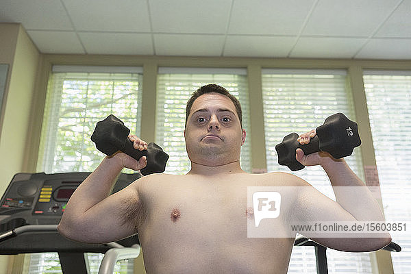 Mann mit Down-Syndrom trainiert in einer Turnhalle mit Hanteln
