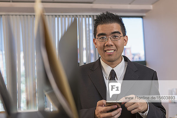 Asiatischer Mann mit Autismus arbeitet in einem Büro mit seinem Telefon