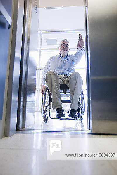 Universitätsprofessor mit Muskeldystrophie im Rollstuhl beim Betreten eines Aufzugs