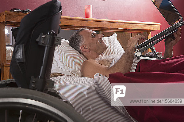 Man with spinal cord injury in the bed using his laptop