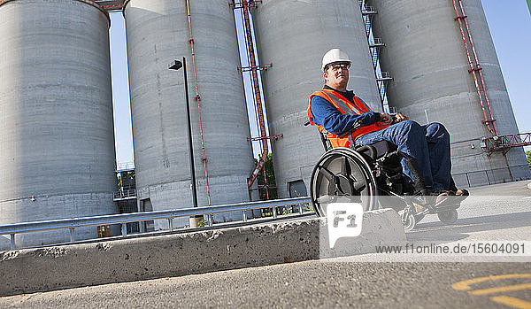 Gebäudetechniker im Rollstuhl bei der Inspektion von Lagertanks für Schüttgut im Freien