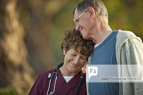 Lächelnde Krankenschwester  die sich zu einem älteren männlichen Patienten im Freien beugt
