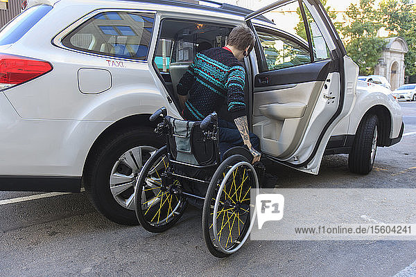 Trendiger Mann mit einer Rückenmarksverletzung im Rollstuhl steigt in ein Taxi ein