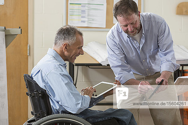 Zwei Projektingenieure nutzen ihre Tablets  um Pläne für die Baustelle zu prüfen  einer sitzt im Rollstuhl und hat eine Rückenmarksverletzung