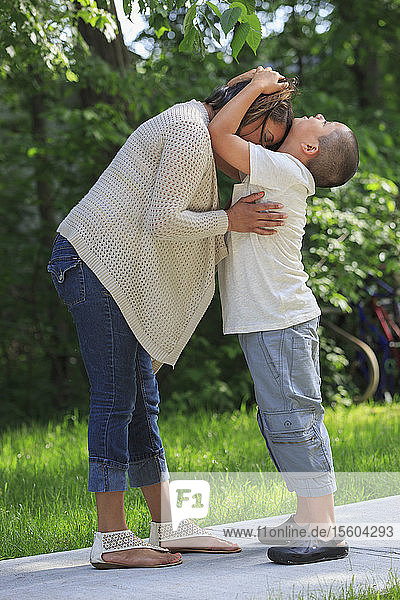 Hispanischer Junge mit Autismus umarmt seine Mutter im Park