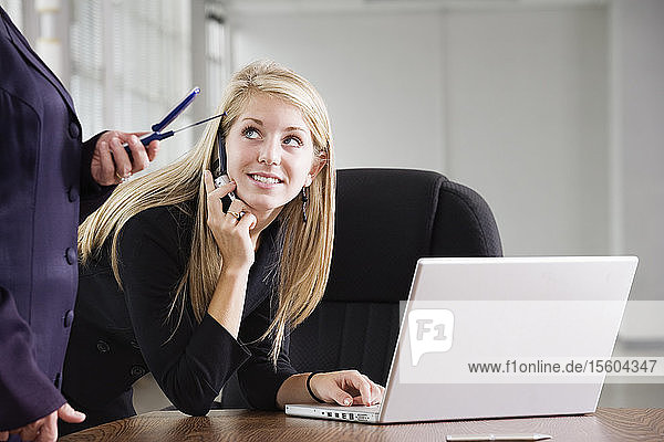 Eine Geschäftsfrau  die ein Mobiltelefon und einen Laptop benutzt.