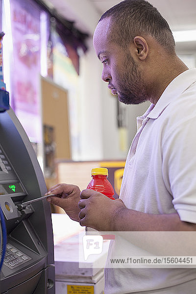 Mann mit Down-Syndrom benutzt einen Geldautomaten in einer Bank