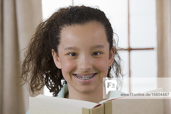 Porträt eines hispanischen Mädchens  das ein Buch liest und lächelt