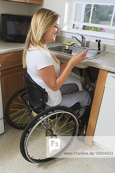 Frau mit Rückenmarksverletzung in ihrer barrierefreien Küche  die ein Mobiltelefon benutzt