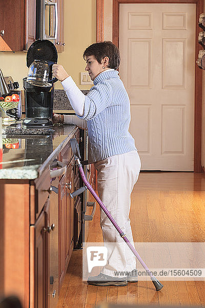 Frau mit Cerebralparese benutzt Krücken und bereitet Kaffee in ihrer Küche zu