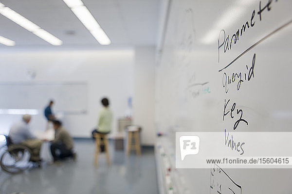 Text auf einem Whiteboard in einem Klassenzimmer mit einem Professor mit Muskeldystrophie im Hintergrund