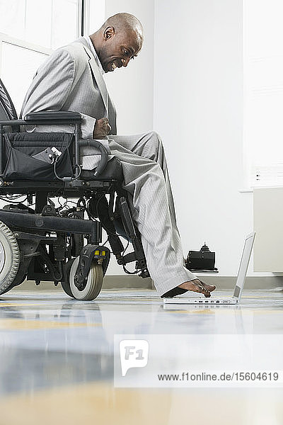 Businessman with Cerebral Palsy sitting in a wheelchair working on a laptop with his foot