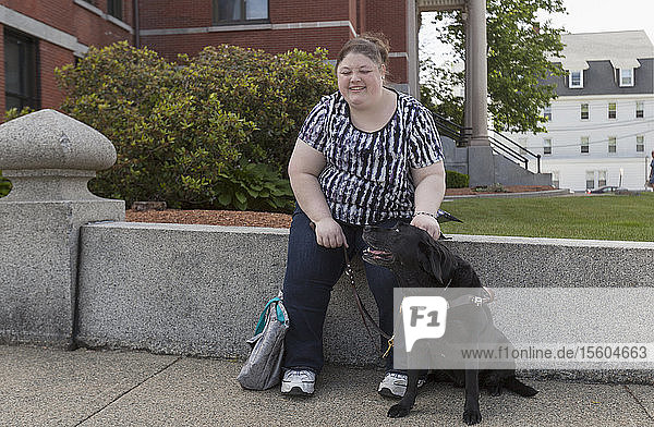 Frau mit Sehbehinderung sitzt mit ihrem Diensthund auf einem Bordstein