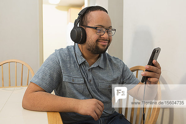 Happy African American man with Down Syndrome listening to music on phone with headphones at home