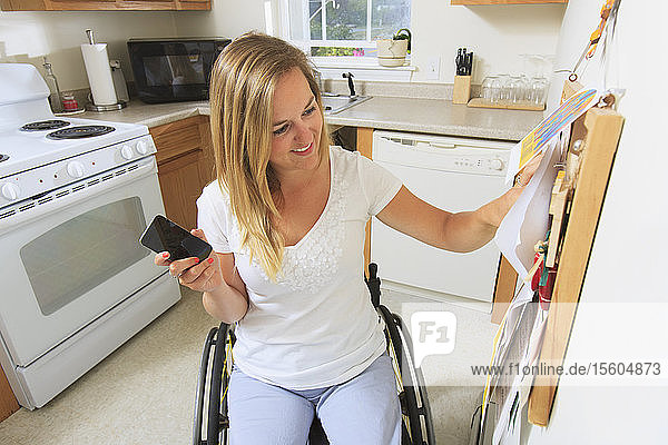 Woman with spinal cord injury in her accessible kitchen looking at notice board