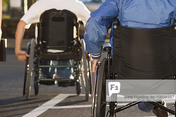 Zwei behinderte Männer  die in Rollstühlen sitzen und die Straße überqueren
