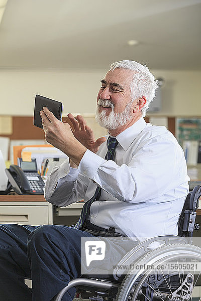 Mann mit Muskeldystrophie im Rollstuhl benutzt ein Tablet an seinem Bürotisch