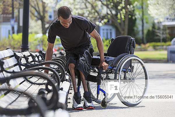 Man who had Spinal Meningitis getting out of a park bench and into his wheelchair