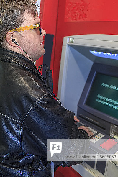 Ein Mann mit angeborener Blindheit benutzt einen Geldautomaten