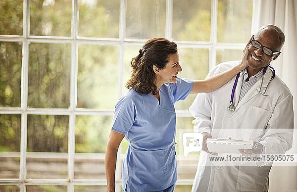 Lachende Ärztin  die ihren männlichen Kollegen spielerisch schubst  während sie zusammen neben einem Fenster stehen