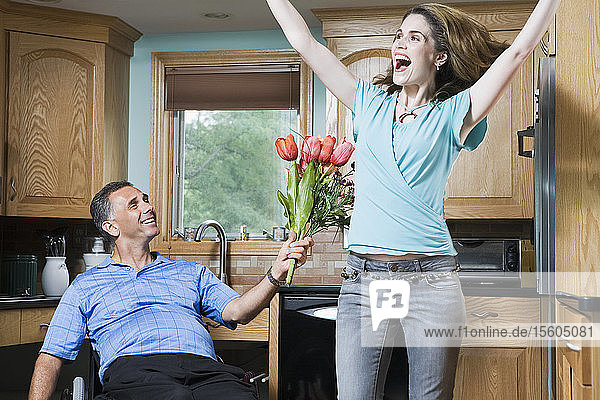 Mittlerer erwachsener Mann im Rollstuhl schenkt einer lachenden mittleren erwachsenen Frau Blumen