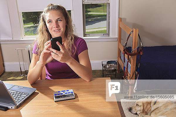 Studentin mit Sehbehinderung benutzt ihr Mobiltelefon in ihrem Wohnheimzimmer
