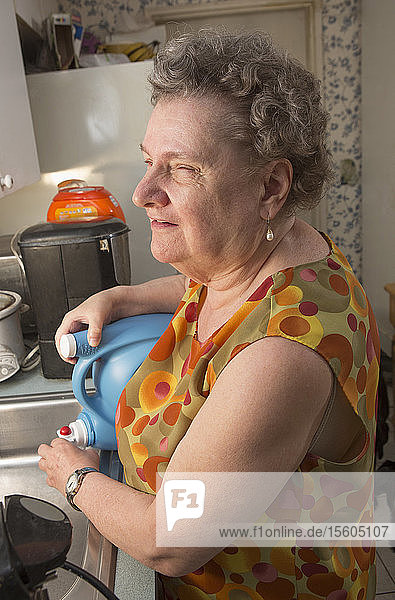 Blind senior woman pouring liquid into her sink in kitchen
