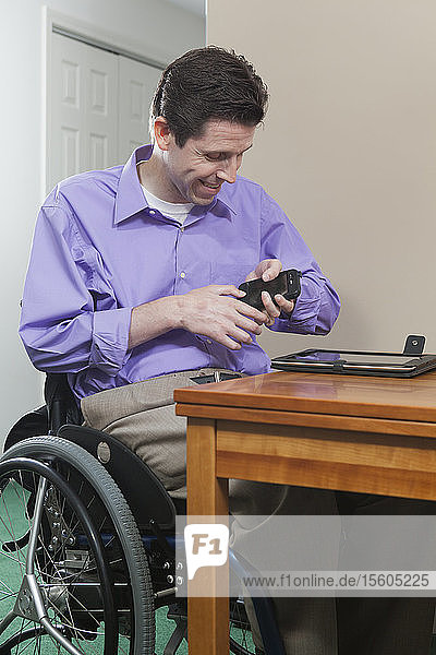 Mann im Rollstuhl mit Rückenmarksverletzung hat Probleme mit der Handgeschicklichkeit bei der Benutzung seines Mobiltelefons