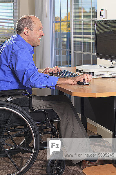 Mann mit Friedreich-Ataxie und deformierten Händen an seinem Computer