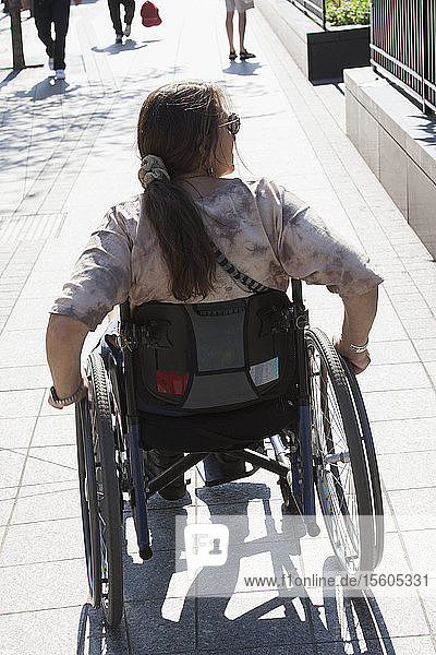 Frau mit Querschnittslähmung im Rollstuhl auf dem Bürgersteig