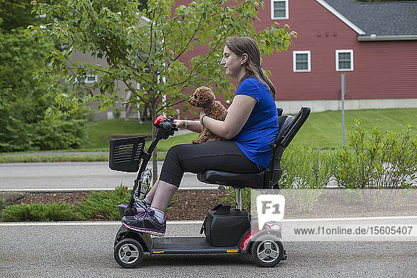 Junge Frau mit zerebraler Lähmung fährt mit ihrem Hund auf dem Roller