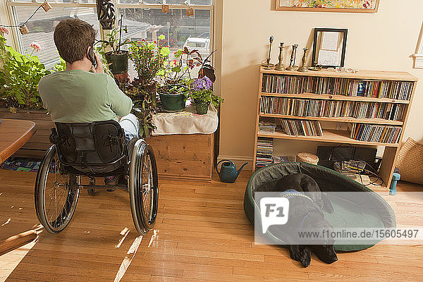 Woman with multiple sclerosis in a wheelchair talking on a mobile phone with service dog sitting near her