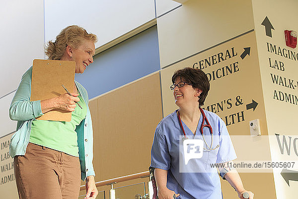 Krankenschwester mit Zerebralparese geht mit einem Verwalter den Flur einer Klinik entlang